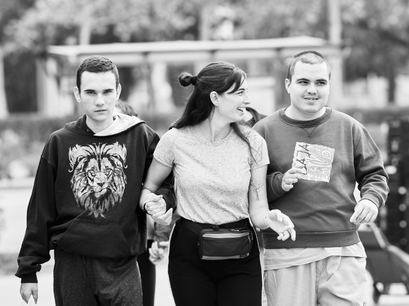 Tres personas, algunas de ellas, con autismo, pasean al aire libre mientras sonríen.