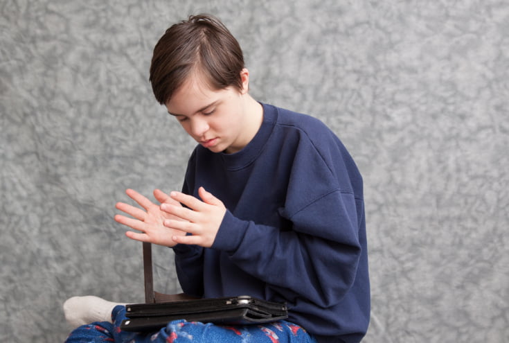 Una persona con autismo aletea sus manos mientras mira hacia sus piernas.