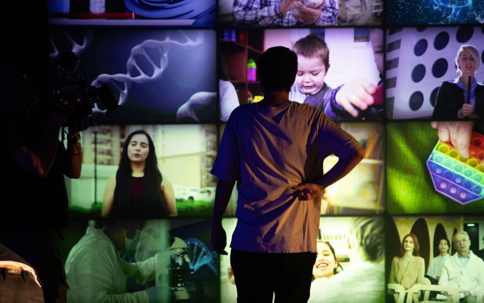 Fotografía en la que una persona que está de espaldas mira hacia un muro lleno de pantallas