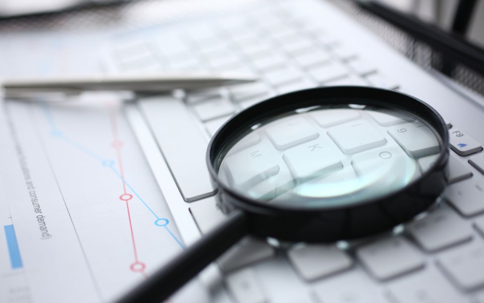 Fotografía con una lupa sobre un teclado de ordenador y documentos en primer plano.