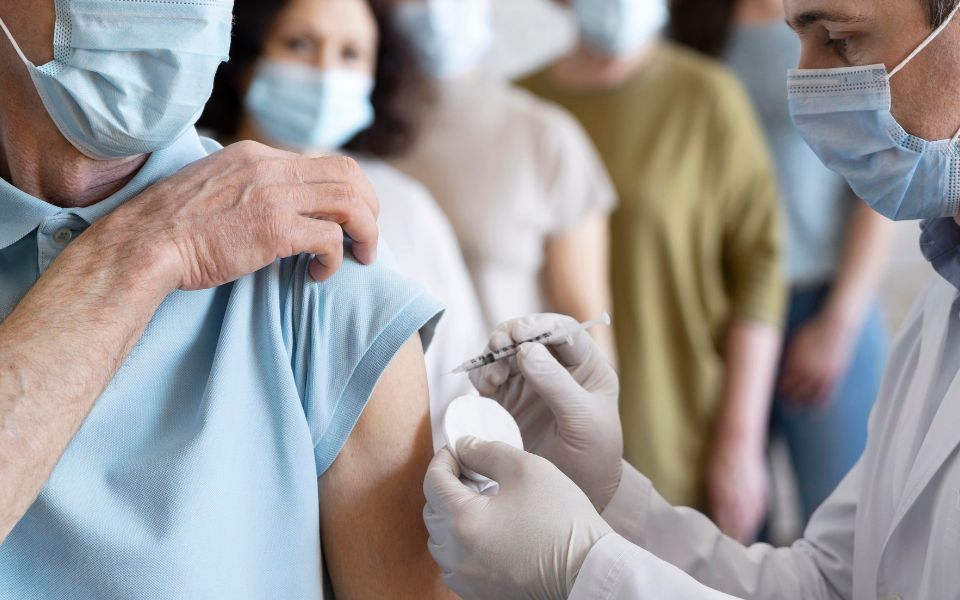 Fotografía en la que una fila de personas esperan para que un médico les ponga una vacuna