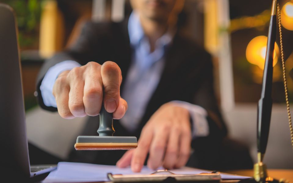 Fotografía en la que una persona va a estampar un sello sobre unos documentos en una oficina.