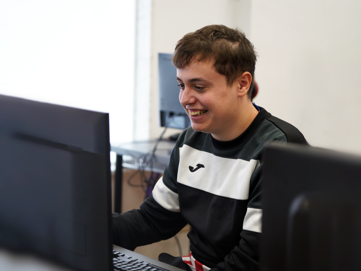 Fotografía en la que un chico observa la pantalla del ordenador mientras sonríe.