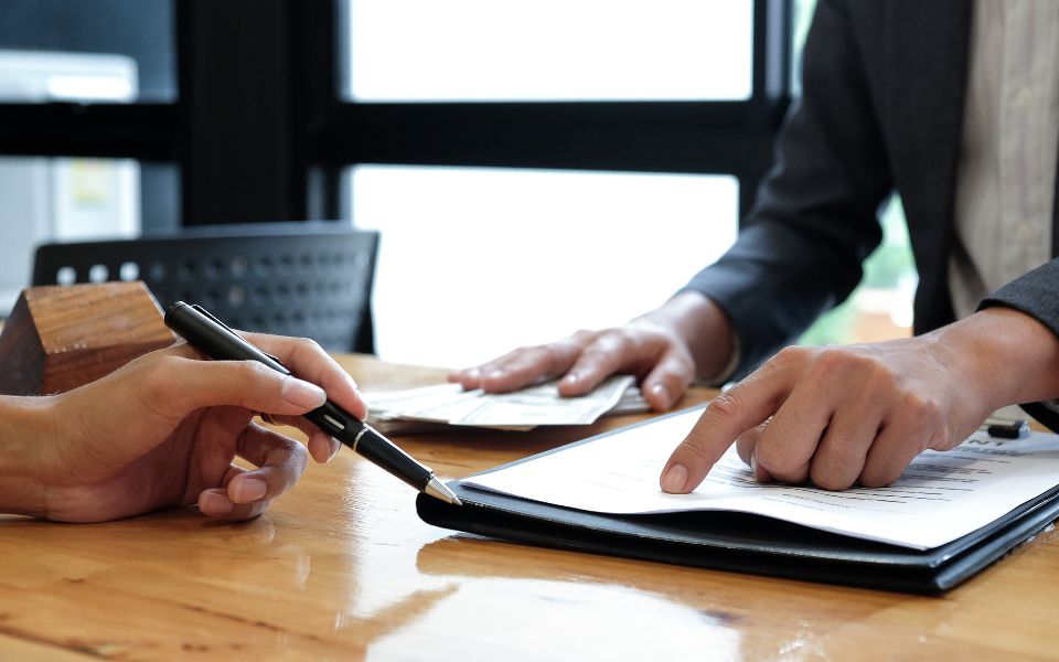 Fotografía: las manos de varias personas comparten documentos que señalan con sus dedos y bolígrafos.