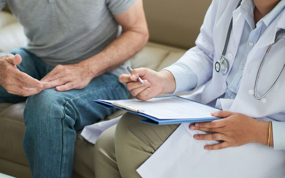 Fotografía de dos personas sentadas en un sofá. una de ellas sostiene una carpeta y apunta con un bolígrafo en un papel.