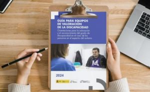 Imagen de una manos sujetando una carpeta donde está la portada de la guía para equipos de valoración de la discapacidad en las personas autistas.
