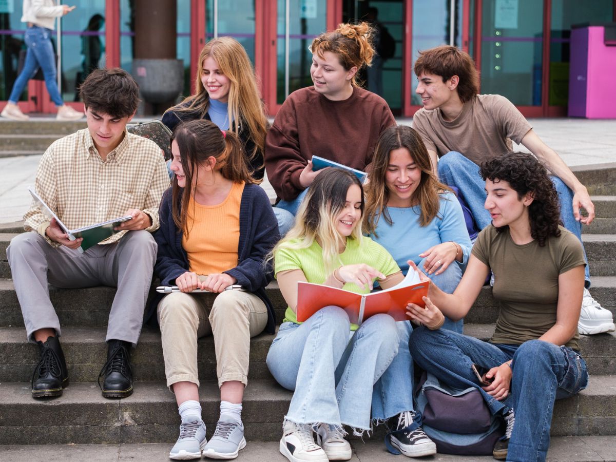 Un grupo de jóvenes comparten información sobre alguna investigación participativa sentados en una escalera.