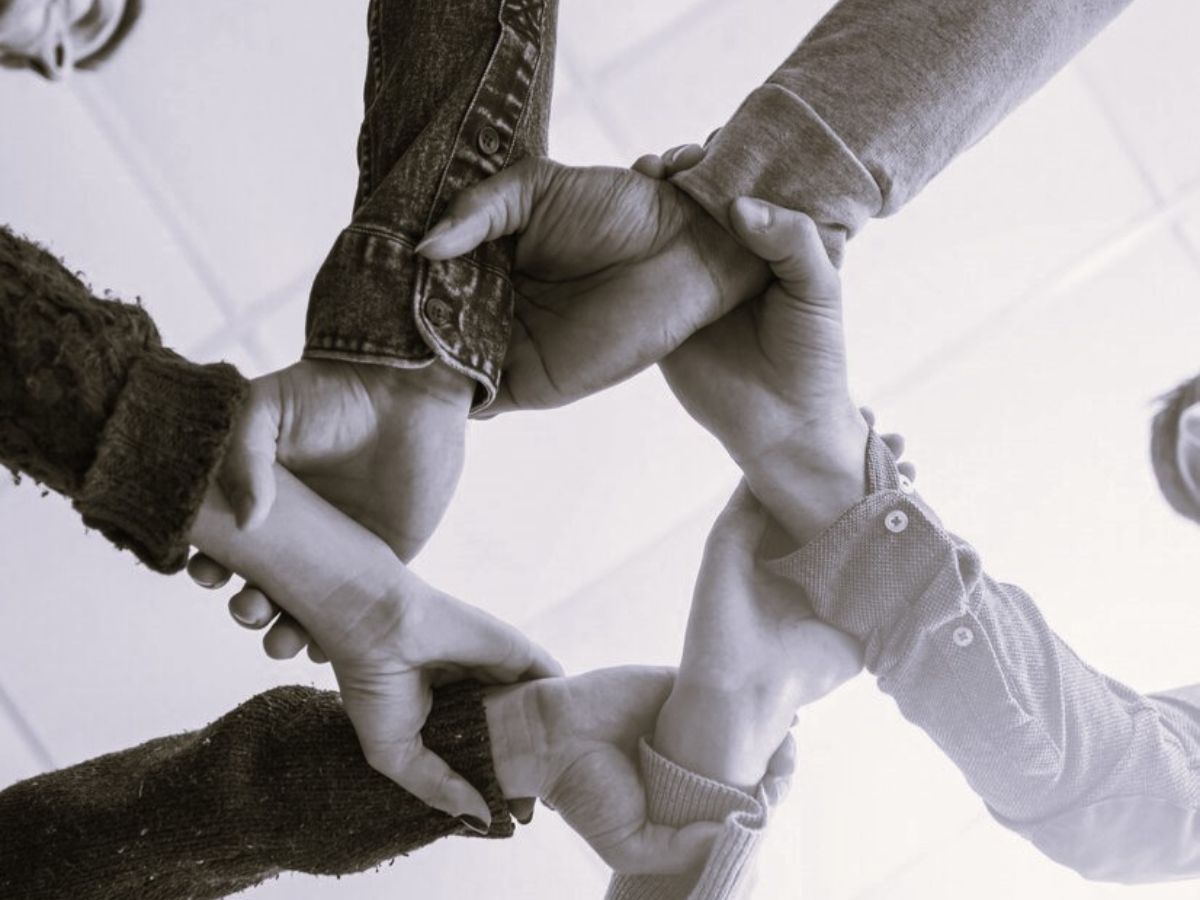 Muchas personas alistas y autistas se cogen de las manos en señal de colaboración durante una investigación participativa.