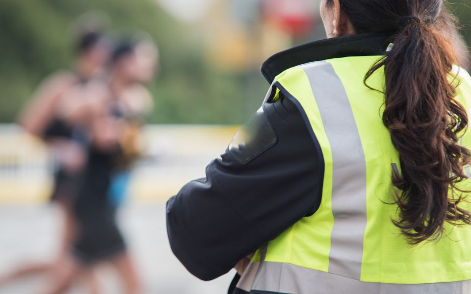 Una agente de seguridad de espalda observa a un grupo de personas que participan en una competición deportiva.